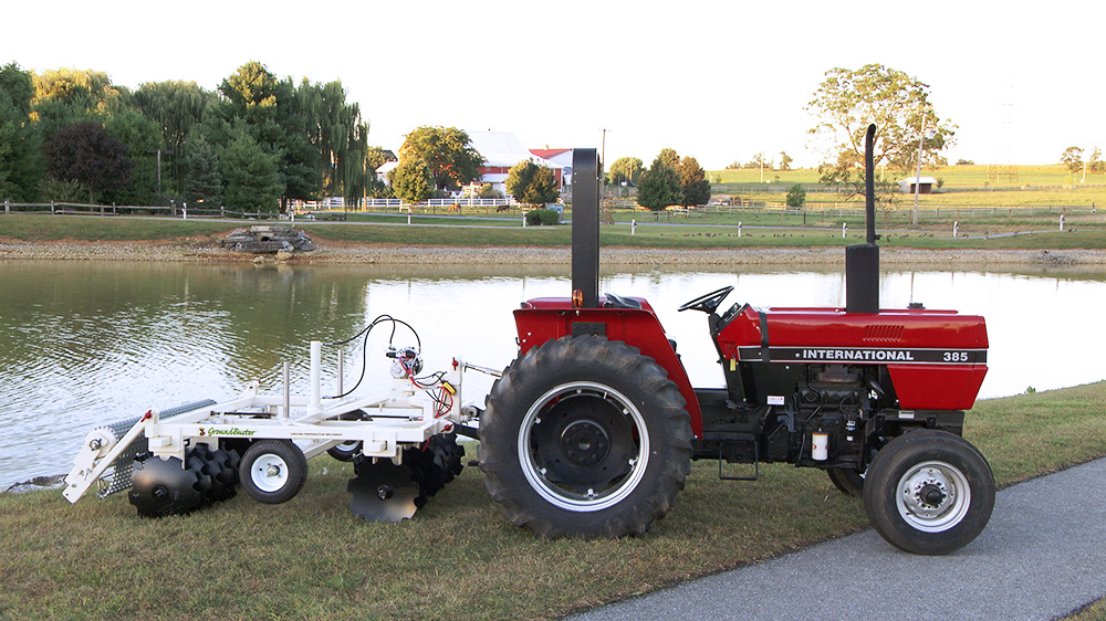 GroundBuster brand tiller attached to red tractor next to pond