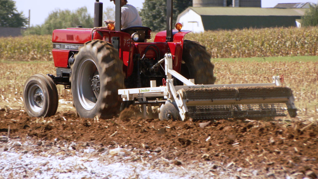 GroundBuster brand tiller attachment pulled by tractor through field